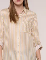 Camisa de corte clásico y silueta relajada con diseño de rayas verticales en blanco y negro. Presenta cuello camisero tradicional, cartera frontal con botones, un bolsillo aplicado en el pecho con rayas horizontales y mangas largas con sistema para arremangar.