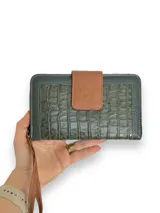 Billetera tipo sobre confeccionada en cuero vacuno color verde con textura tipo cocodrilo. Tiene cierre perimetral con cremallera, correa de mano desmontable y broche de cuero marrón con logo de la marca.