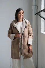 Tapado tipo gamuza con interior de corderito sintético, color beige con detalles en crudo. Presenta capucha, cierre frontal completo y puños con vuelta de corderito.