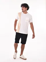Remera de corte oversize, con diseño bicolor que combina blanco y beige. Presenta un bolsillo frontal en el pecho con el logo de la marca bordado y una etiqueta pequeña en el ruedo.
