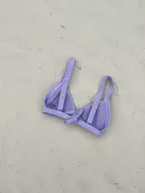 Top de bikini modelo triángulo en color lila, con textura acanalada y breteles regulables. Cuenta con forro interno y cierre mediante atadura en la espalda.