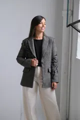 Blazer de corte sastrero en color gris con patrón de rayas diagonales y bordados negros en las mangas y solapas. Presenta cierre frontal con botón, bolsillos con solapa y estructura clásica.