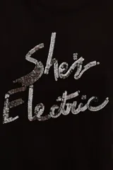 Remera de viscosa color negro, de corte clásico y manga corta, con estampa frontal de texto bordada en lentejuelas plateadas.