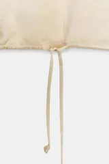 Camisa de cuello solapa y manga larga con puños anchos, confeccionada en tejido satinado color beige. Presenta cierre frontal con botones ocultos y bajo ajustable mediante cordones del mismo tejido.