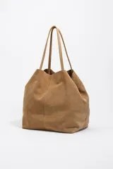 Bolso shopper grande de Bimba y Lola, confeccionado en serraje de piel vacuna con acabado de ante color marrón. Presenta doble asa de hombro y detalle de logo metálico de la marca en la parte inferior.