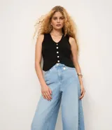 Pantalón de jean estilo pantalona con cintura alta, corte amplio desde el cuadril y cinco bolsillos funcionales. Presenta cierre frontal con botón y cremallera, además de un detalle de charm metálico en la cintura.