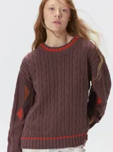 Sweater de tejido de punto trenzado en color marrón, con cuello redondo, puños y ruedo acanalados. Presenta detalles de franjas en color naranja en el cuello y el ruedo, además de apliques de rombos en tonos naranja y verde en las mangas.
