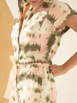 Mono corto con estampado tie-dye en tonos rosa, blanco y verde. Presenta cuello camisero, mangas cortas con dobladillo, cierre frontal con botones y cinturón de lazo.