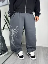 Pantalón de jogging gris oscuro de corte oversize con diseño holgado. Cuenta con un gran estampado caligráfico en color blanco en la pierna derecha.