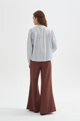 Blusa de algodón color beige, con cuello redondo y cierre frontal con botones. Presenta delicados bordados decorativos en tono tostado sobre el pecho y los hombros, mangas largas abullonadas con puños ajustados y diseño holgado.