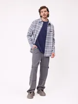 Camisa de manga larga con estampado de cuadros en tonos blanco, gris y azul. Presenta cuello clásico, cierre frontal con botones y un pequeño parche con logo en el pecho.