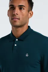 Polo de manga larga color verde oscuro (teal) con cuello polo y tapeta de dos botones. Presenta un pequeño logo bordado de pingüino en el pecho.