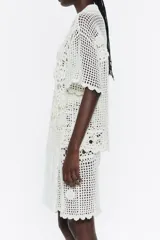 Camisa de crochet color blanco, con cuello camisero, manga corta y cierre frontal con botones.