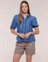 Camisa de lyocell color azul con efecto denim, cuello camisero, cierre frontal con botones y detalles de bordado oscuro a lo largo de la botonera. Presenta mangas cortas abullonadas con puños elásticos y terminación con volados.
