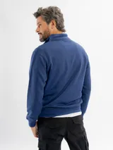 Buzo de felpa color azul, con cuello alto y cierre frontal parcial, mangas largas y puños elásticos.