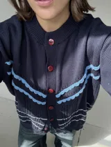 Saco de punto color crema con detalles en crochet verde, cierre frontal con botones y mangas largas.