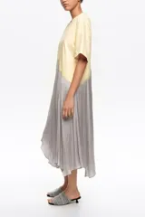 Vestido midi de línea A con diseño bimateria. Parte superior de tejido de algodón color amarillo claro con escote redondo y mangas cortas, y parte inferior de tejido satinado gris con caída fluida. Cuenta con detalle de encaje superpuesto en la unión con acabado irregular.