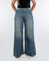 Pantalón de jean de tiro medio y corte wide leg, con diseño de cinco bolsillos y acabado desgastado vintage. Presenta costuras verticales en el frente de las piernas y ruedo desflecado.