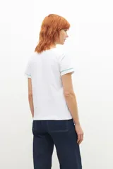 Remera blanca de manga corta con cuello en V, adornada con un bordado floral en color verde menta en el área del pecho y ribetes del mismo color en el cuello y mangas.