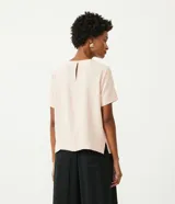 Blusa blanca de poliéster de corte recto, con cuello redondo, mangas cortas con dobladillo y detalles de pespuntes a contratono.