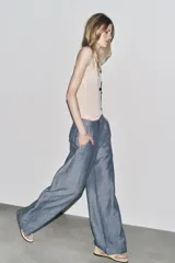 Pantalón de tiro bajo color azul con textura de lino, de pierna ancha, con bolsillos delanteros y traseros. Cierre frontal con cremallera, botón y ganchos metálicos.