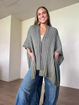 Ruana tejida de algodón con hilo lurex en punto jersey, color azul, con diseño amplio y detalle de etiqueta de cuerina en la parte posterior.