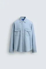 Camisa de corte regular confeccionada en tejido de algodón con efecto lavado. Presenta cuello solapa, manga larga con puños abotonados, cierre frontal de botones y dos bolsillos de plastrón con solapa en el pecho.