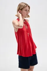 Musculosa de viscosa color rojo, con cuello halter, corte ajustado al cuerpo y detalle de cordones con cuentas en el escote.
