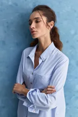 Camisa celeste de calce relajado, con cuello camisero, bolsillo aplicado en el pecho y mangas largas con puños abotonados. Cuenta con lazos ajustables en los laterales para fruncir y regular la silueta.
