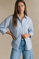 Camisa de corte oversize con estampado de rayas verticales en tonos azul y beige. Presenta cuello camisero clásico, cierre frontal con botones, bolsillo en el pecho y mangas largas con puños rectos.