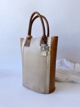 Bolso matero de cuero color beige con textura de reptil y detalles en cuero marrón con textura de cocodrilo. Incluye manijas cortas de cuero marrón y dije de cruz plateada.