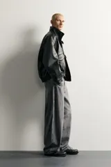 Cazadora relaxed fit de tejido efecto piel en color negro, con cuello subido, manga larga, bolsillos con solapa en el delantero y acabados elásticos. Cierre frontal con cremallera oculta por solapa.