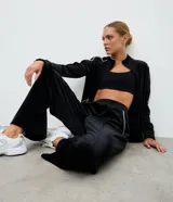 Pantalón deportivo de corte recto confeccionado en plush negro, con cintura elástica y detalle de piping blanco en los laterales.