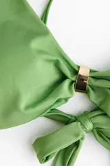 Top de bikini verde con tirantes ajustables, copas con relleno extraíble, frunces en los laterales, detalle metálico en el centro y tiras para anudar en la espalda.