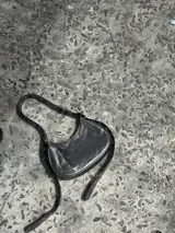 Bolso de hombro tipo media luna, color peltre (gris metálico), con acabado en cuero semi quebrado. Presenta detalles de ojales metálicos niquelados en las asas y correa regulable.