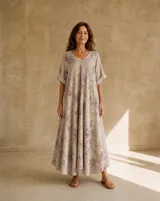 Vestido largo beige con estampado floral en tonos rosados y grises, escote en V y mangas cortas holgadas.