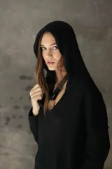 Sweater de punto negro con capucha, diseño de manga larga y corte holgado. Presenta un detalle de argolla metálica en el escote.