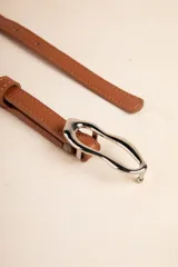 Cinturón fino color marrón de símil cuero con hebilla metálica irregular plateada.