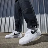 Championes Nike Air Force 1 de corte bajo, color blanco con detalles en textura de piel de serpiente en tono bronce en el swoosh lateral y en el talón.