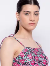 Top corto con escote recto y tirantes finos ajustables mediante nudo en los hombros. Presenta un estampado floral sobre fondo oscuro, con flores rosadas y hojas turquesas.