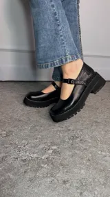 Guillerminas Mathi de color negro, con plataforma robusta, suela dentada y pespuntes blancos. Tienen una tira en el empeine con hebilla metálica y combinación de texturas.
