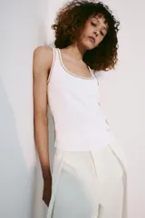 Musculosa de algodón color blanco con cuello redondo amplio y sisas. Cuenta con detalles de ribetes dorados brillantes en el escote, tirantes y costuras laterales.