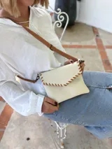 Cartera tipo sobre color crudo, confeccionada en cuero, con correa larga de cuero marrón y costuras decorativas en contraste.