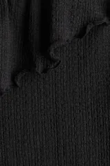 Top negro de punto texturizado con un solo hombro y volado ancho en el escote. Diseño ajustado con ribetes sobrehilados.