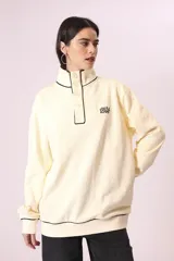 Buzo color crema con cuello alto abotonado y puños con ribete negro.