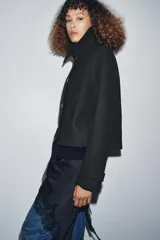 Abrigo corto de lana con cuello solapa, cierre frontal de botones y mangas largas ajustables con trabilla y botón. Cuenta con bolsillos delanteros y forro interior a tono.