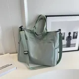 Bolso tipo tote y shopper de color negro, confeccionado en poliéster con amplio espacio interior, doble asa de mano y correa larga ajustable para llevar al hombro o cruzado.