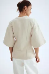 Top de punto fino con cuello redondo, hombros caídos y mangas al codo. Presenta costuras decorativas verticales en el frente y un bajo levemente acampanado con corte holgado.