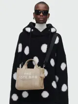 Cartera tipo tote de Marc Jacobs, modelo The Small Tote Bag, color beige con letras blancas estampadas en el frente. Cuenta con doble asa superior y correa de hombro ajustable y extraíble.