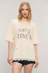 Remera oversize de jersey de algodón en color blanco, con cuello redondo, mangas cortas y largo a la cadera. Presenta estampa frontal con la inscripción "Gypsy Lover", detalles de roturas y apliques de puntilla en las mangas y el ruedo.